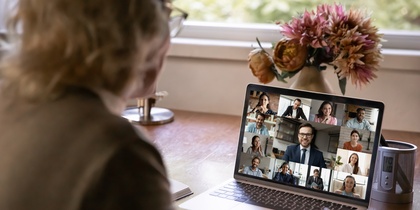 En person deltar i ett videomöte med flera deltagare på en bärbar dator vid ett skrivbord.