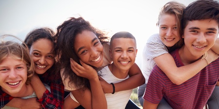 Sex ungdomar utomhus, två ger ryggsäckar till sina vänner, alla ler mot kameran.