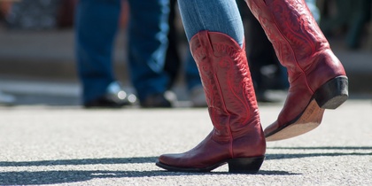Person i blå jeans och röda cowboyboots dansar utomhus på asfalt.