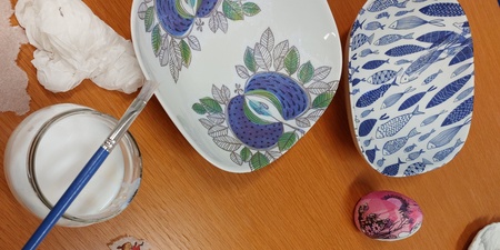 Person dekorerar porslin med decoupage och små figurer på ett träbord.