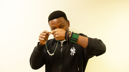 Man i svart hoodie visar upp halsband och armband mot ljus bakgrund.