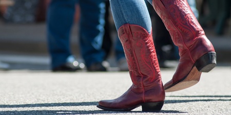 Person i blå jeans och röda cowboyboots dansar utomhus på asfalt.