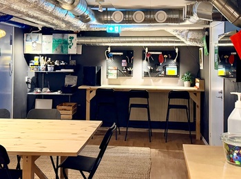 Ett modernt, färgglatt hobbyrum med arbetsbord, stolar, ventilationsrör i taket och pysselmaterial på bänkar.