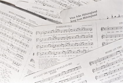 Flera noter och sångblad ligger utspridda, med både svensk och engelsk text.