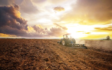 En traktor plöjer en åker vid solnedgången under en dramatisk himmel.