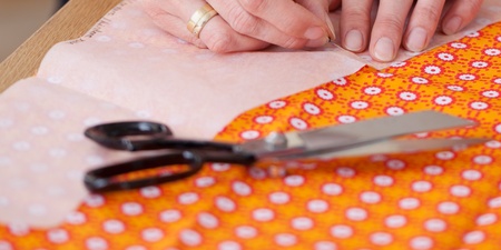 Händer som nålar fast mönsterpapper på orange tyg med sax och krita bredvid.