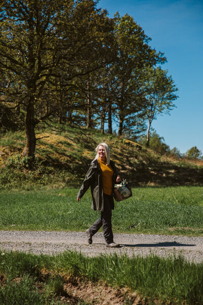 Kvinna promenerar på en grusväg i naturen under en solig dag, omgiven av grönt gräs och träd.