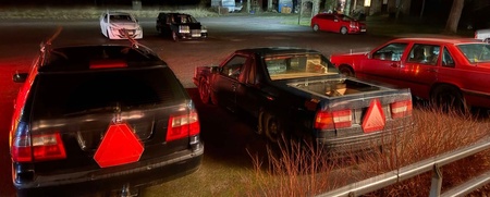 Flera bilar står parkerade på en mörk parkeringsplats, alla med röda trianglar bakpå.