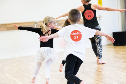 Barn och en vuxen dansar tillsammans i en ljus dansstudio med trägolv.