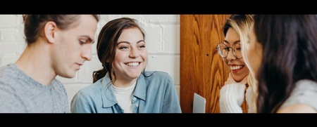 Fyra unga vuxna sitter tillsammans och samtalar, två av dem ler mot varandra.