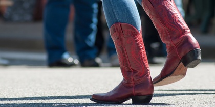 Person i blå jeans och röda cowboyboots dansar utomhus på asfalt.