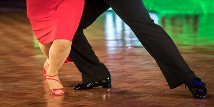 Två personer dansar tillsammans på ett dansgolv, endast deras ben och fötter syns.