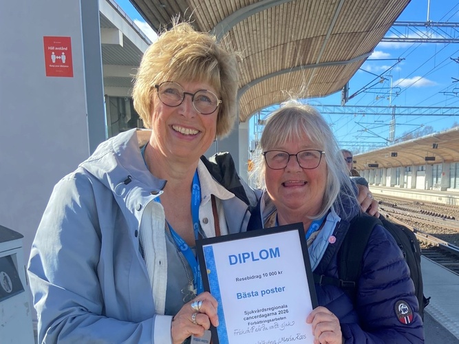 Två personer står på en tågperrong och håller ett diplom för bästa poster.