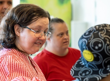 En grupp personer, några med Downs syndrom, står tillsammans inomhus och samtalar.