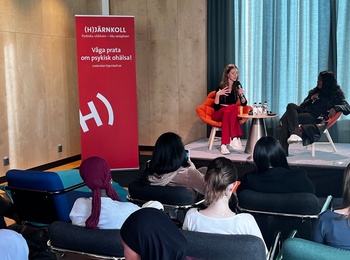 En liten publik lyssnar på två personer som samtalar på en scen i ett modernt konferensrum.