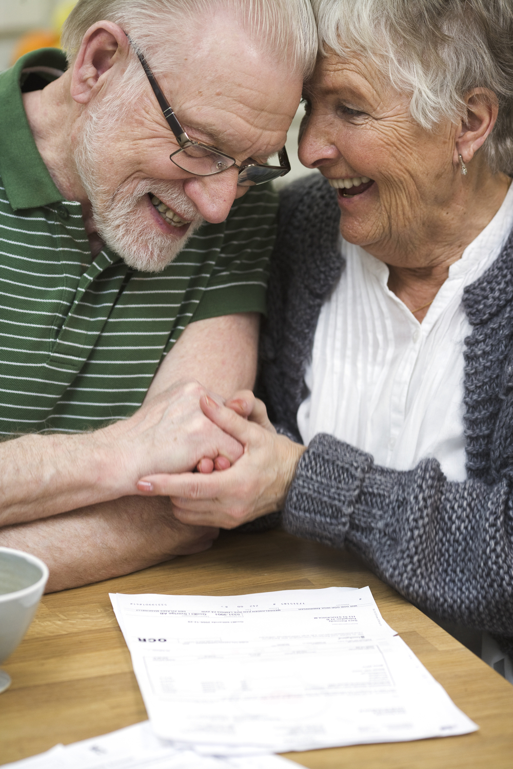 Ett äldre par sitter vid ett bord, håller varandra i händerna och ler mot varandra.
