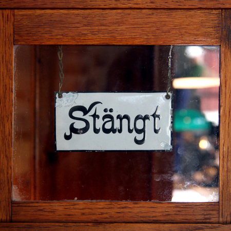 En skylt med texten 'Stängt' hänger på en glasdörr med träram.