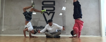 Tre personer i dansstudio, två gör huvudstående poser medan en sitter i mitten på golvet.