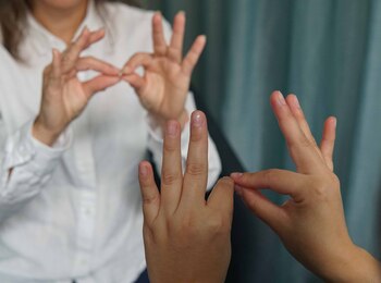 Två personer kommunicerar med teckenspråk, fokus på deras händer mot en suddig bakgrund.