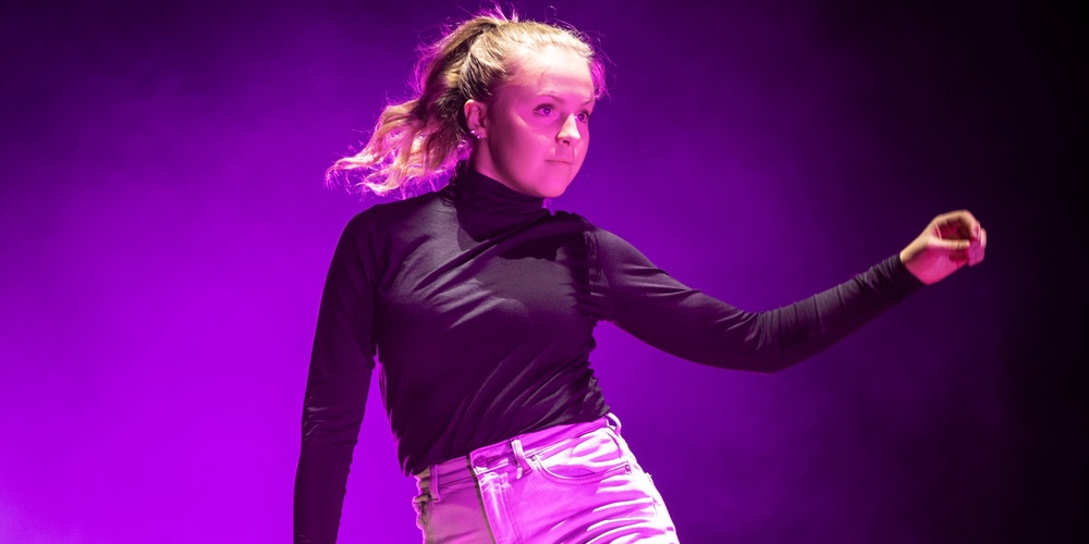 En person dansar barfota på en scen med lila ljus och rökeffekter.