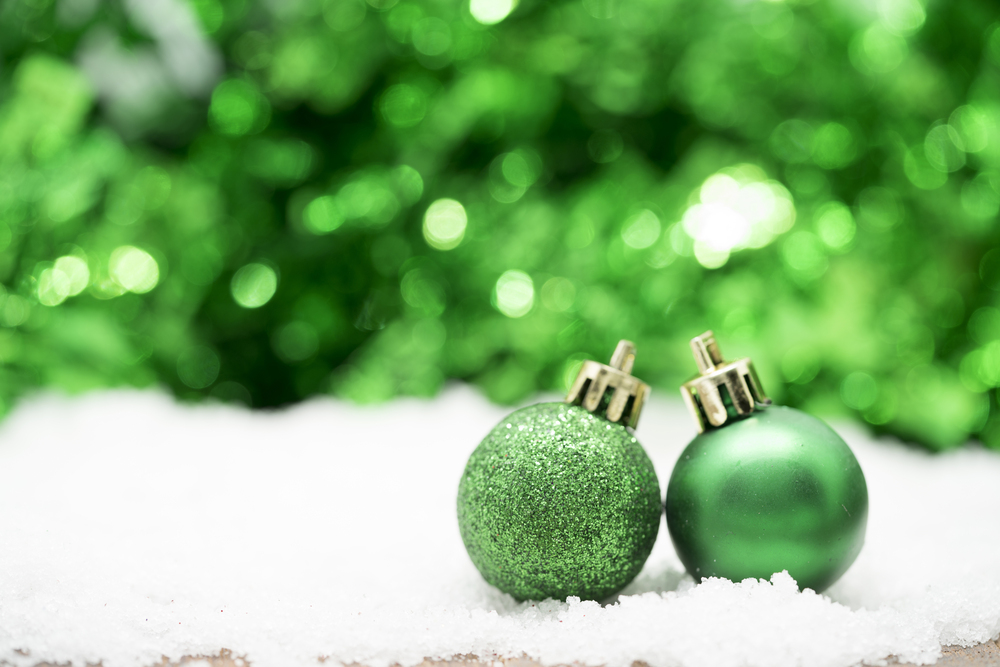 Två gröna julgranskulor står på konstsnö med suddig grön bakgrund.
