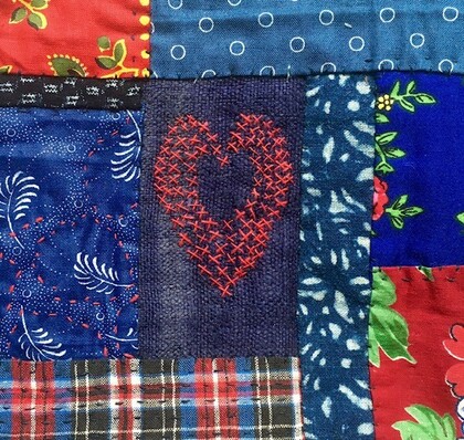Närbild av ett lapptäcke med färgglada tygbitar och ett rött broderat hjärta i mitten.