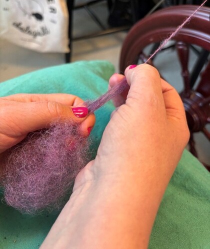 Närbild på händer som spinner lila ull till garn med en spinnrock.