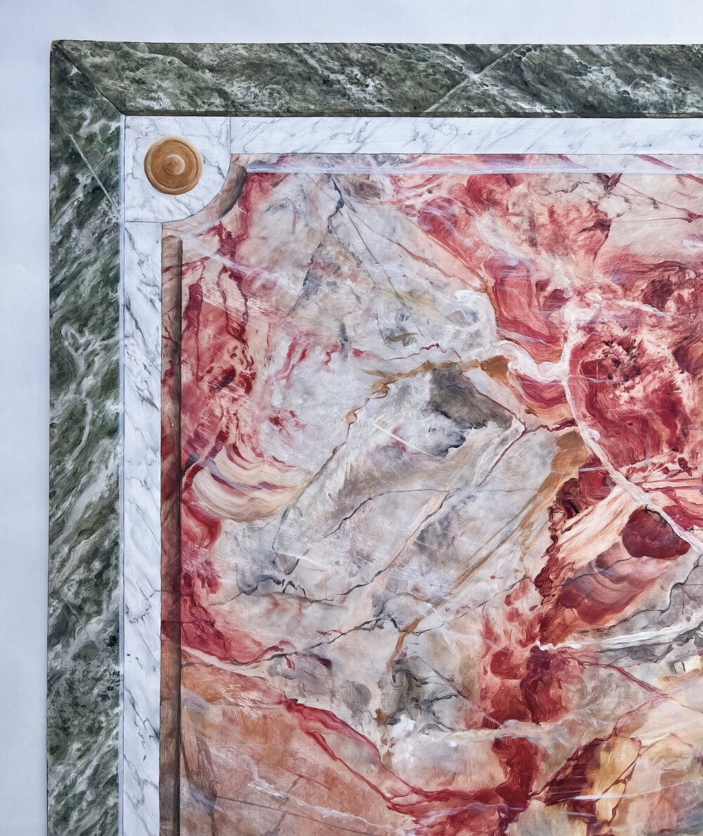 Närbild av en marmorerad yta med gröna, vita och röda färger samt dekorativ ram.