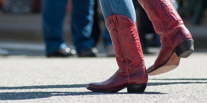 Person i blå jeans och röda cowboyboots dansar utomhus på asfalt.