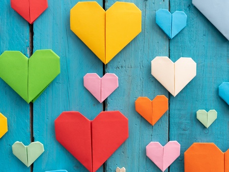 Flera färgglada origamihjärtan i olika storlekar på en blå träbakgrund.
