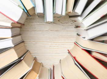 Böcker placerade i en cirkel med ett hjärtformat tomrum i mitten på ett ljust träbord.