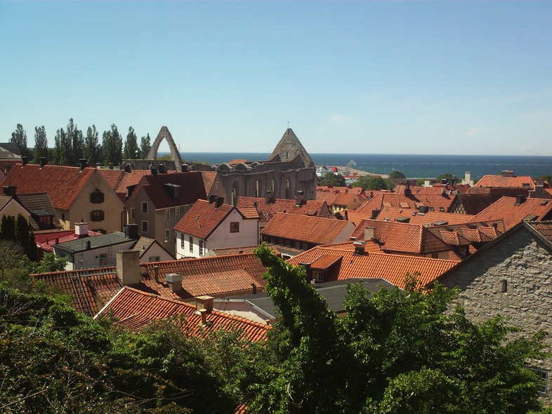 Utsikt över en stad med röda tegeltak, gamla byggnader och havet i bakgrunden under en klar himmel.