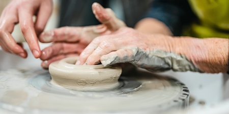 Två par händer formar lera på en drejskiva under en keramikkurs.