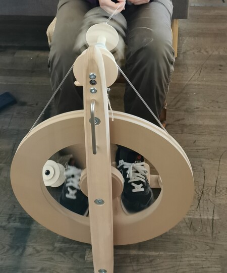 Person spinner garn med en spinnrock, sedd ovanifrån. Fötterna syns på tramporna.