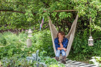 Person sitter i en hängstol under ett träd i en grönskande trädgård med lyktor och vimplar.