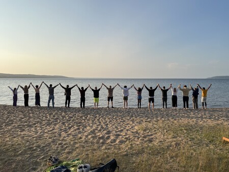 En grupp människor står i rad på en strand med armarna uppsträckta mot himlen vid vattnet.