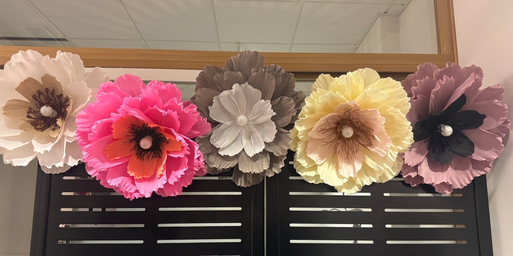 Fem stora, färgglada pappersblommor sitter fast på en svart skärm framför en spegel.