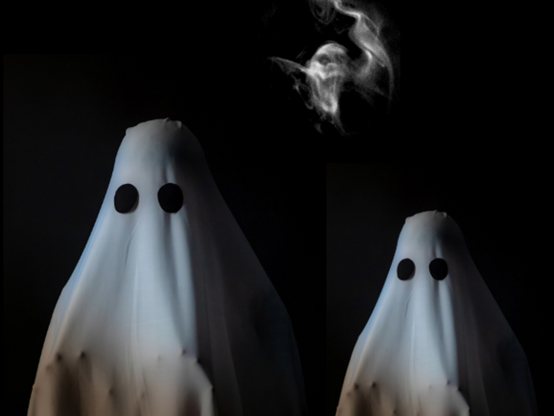 Tre personer utklädda till spöken med vita lakan och svarta ögon på en mörk bakgrund.