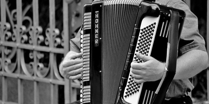 En person spelar dragspel utomhus, bilden är i svartvitt och visar endast överkroppen och instrumentet.