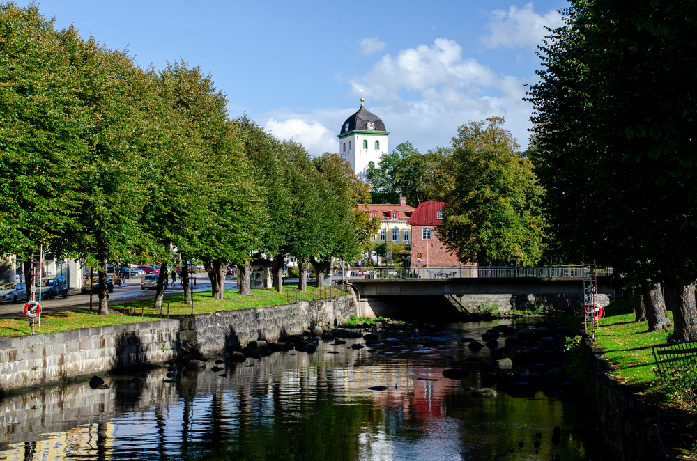 En lugn stadskanal med träd längs sidorna, en bro och en vit kyrka med svart tak i bakgrunden.