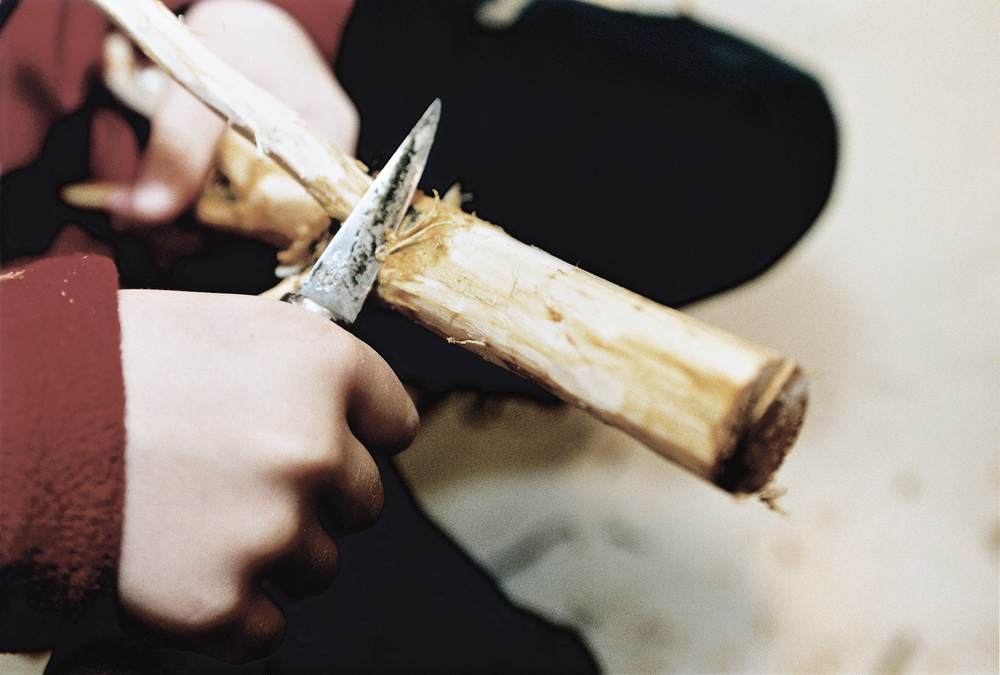 En person täljer en träpinne med en kniv, närbild på händer och trä.