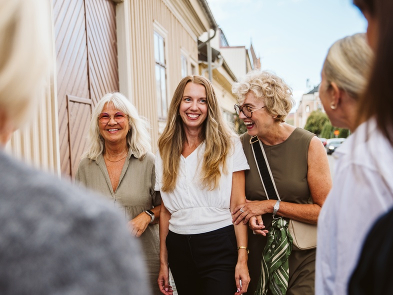 Tre kvinnor går arm i arm och ler
