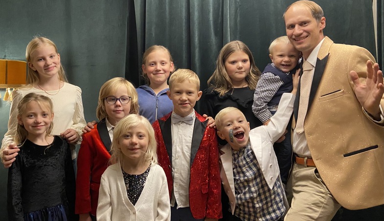 En grupp barn och en vuxen man poserar tillsammans, alla är finklädda och ler mot kameran.