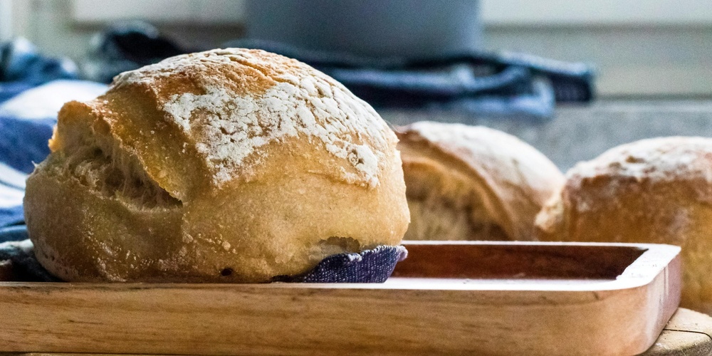 Nybakat bröd ligger på en träbricka i ett kök med suddig bakgrund.