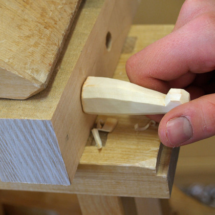 En hand sätter in en träkil i en träfog på en arbetsbänk.