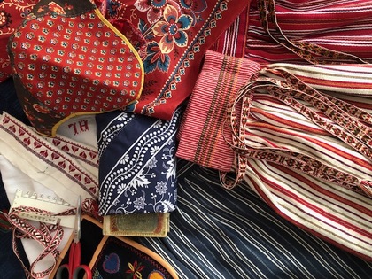 Närbild av traditionella textilier och band i rött, blått och vitt med broderier och mönster.
