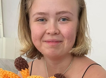 Ung kvinna sitter i soffa och håller i en stickad giraff-leksak, ler mot kameran.
