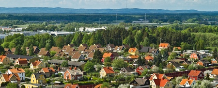 Färgglada villor med röda och gula tak i ett lummigt bostadsområde, omgivna av skog och berg i bakgrunden.