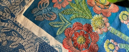 Färgglada broderade tyger med blommor och fåglar samt två rullar garn i rött och grönt.