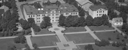 Flygfoto i svartvitt över en stor byggnad med park och gångvägar framför.